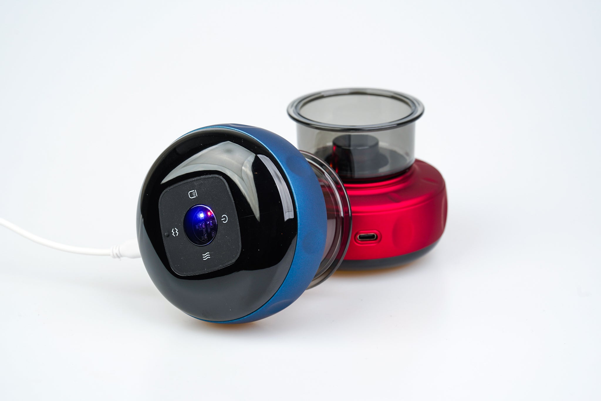 En sort og blå Smart Cup Basic robotstøvsuger placeret ved siden af en rød elkedel på en almindelig hvid baggrund. Støvsugeren har en synlig tænd/sluk-knap og blåt indikatorlys, der repræsenterer et rent nordisk design.